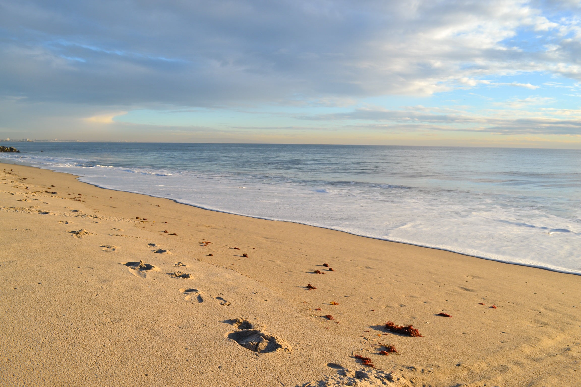 Calm waves on a yellow, brown sandy seashore. Blue sky and white clouds above.